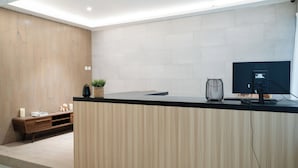 A modern reception desk with a wooden finish, a black countertop, and a computer monitor. - ARA Stay By ARBA (Bandung)