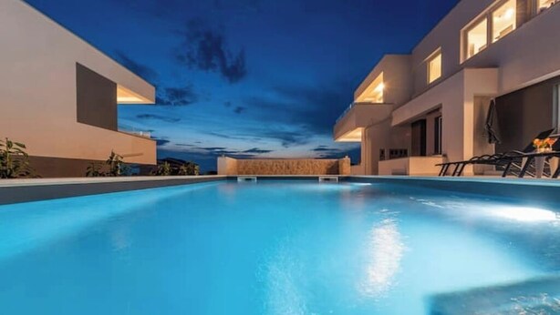 Uma área de piscina moderna com céu claro ao entardecer, rodeada por edifícios com janelas amplas e mobiliário de exterior.