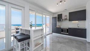 Uma cozinha moderna com vista para o mar, banquetas brancas e uma janela ampla.
