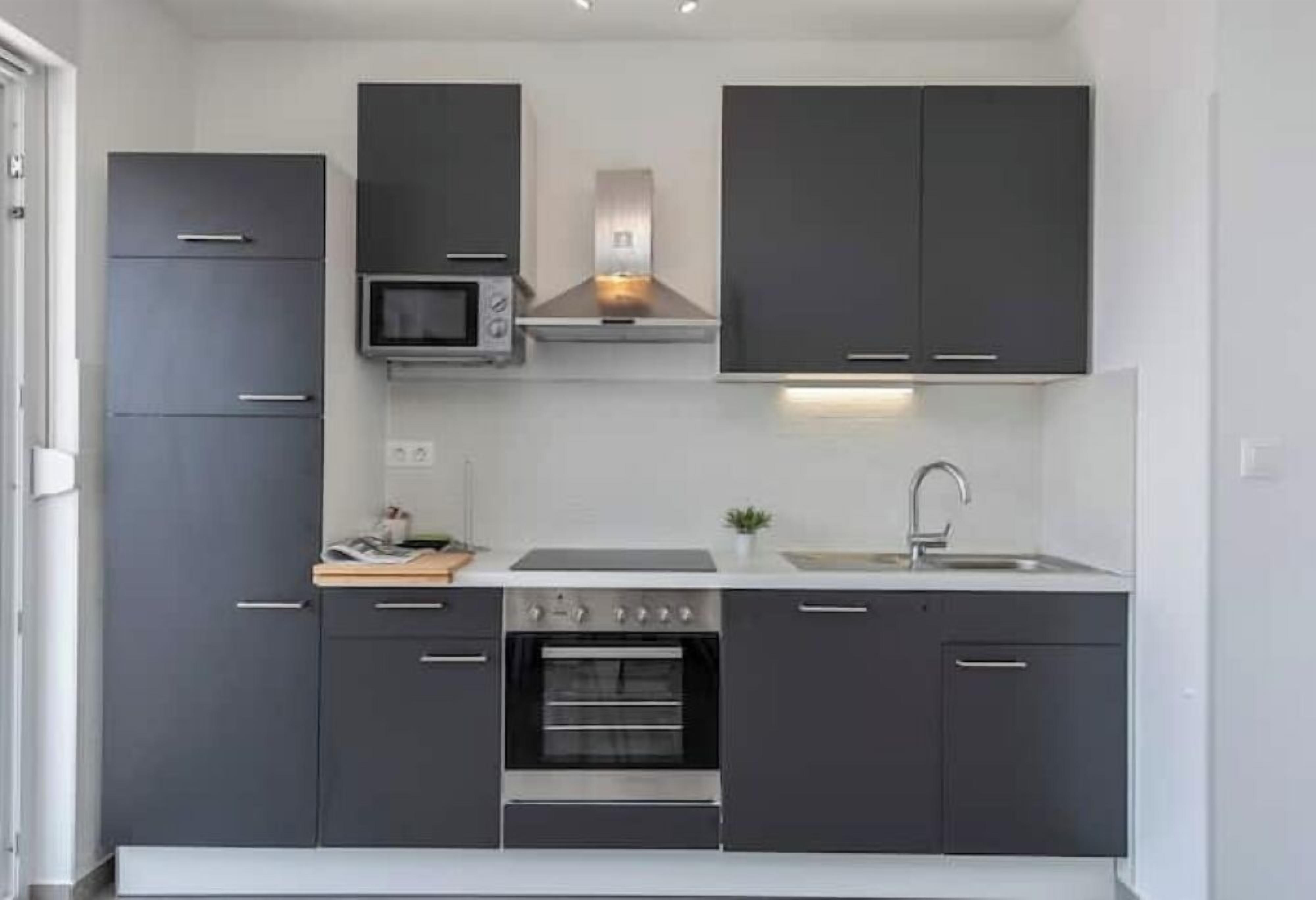 Une cuisine de taille réduite, dotée de meubles de rangement sombres, d’un four à micro-ondes, d’une cuisinière et d’un évier.