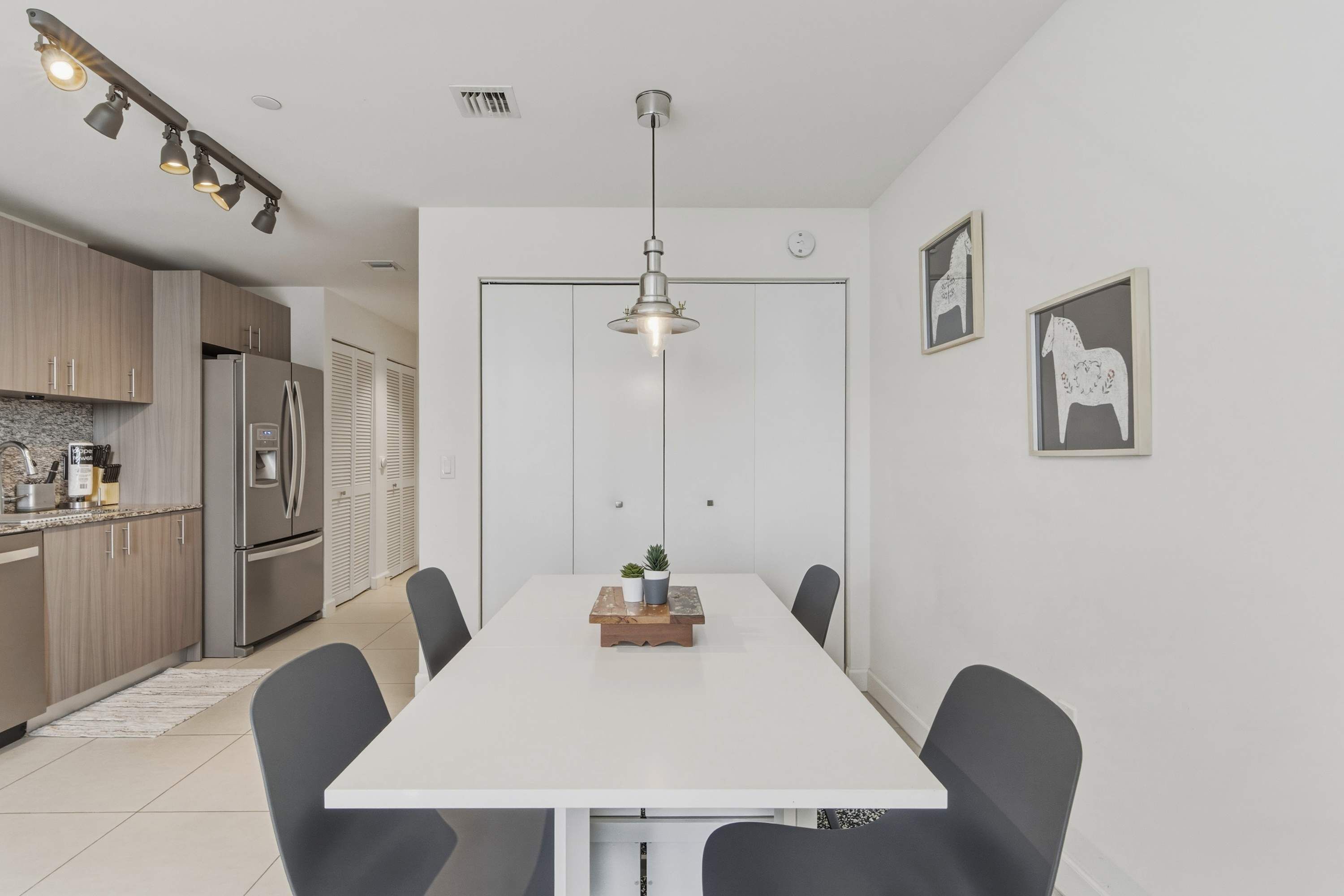 A modern kitchen with stainless steel appliances, a dining area with a white table and black chairs, and a pendant light above the table.