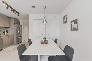 Eine moderne Küche mit Edelstahlgeräten, ein Essbereich mit weißem Tisch und schwarzen Stühlen sowie eine Pendelleuchte darüber.