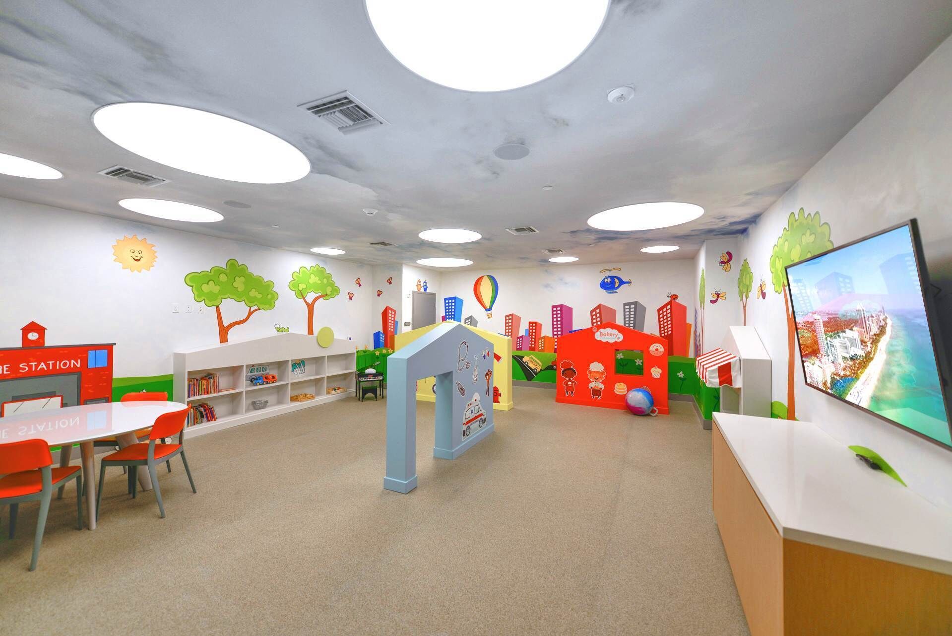 A children's play area with colorful play structures, a bookshelf, and a television screen.
