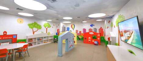 A children's play area with colorful play structures, a bookshelf, and a television screen.