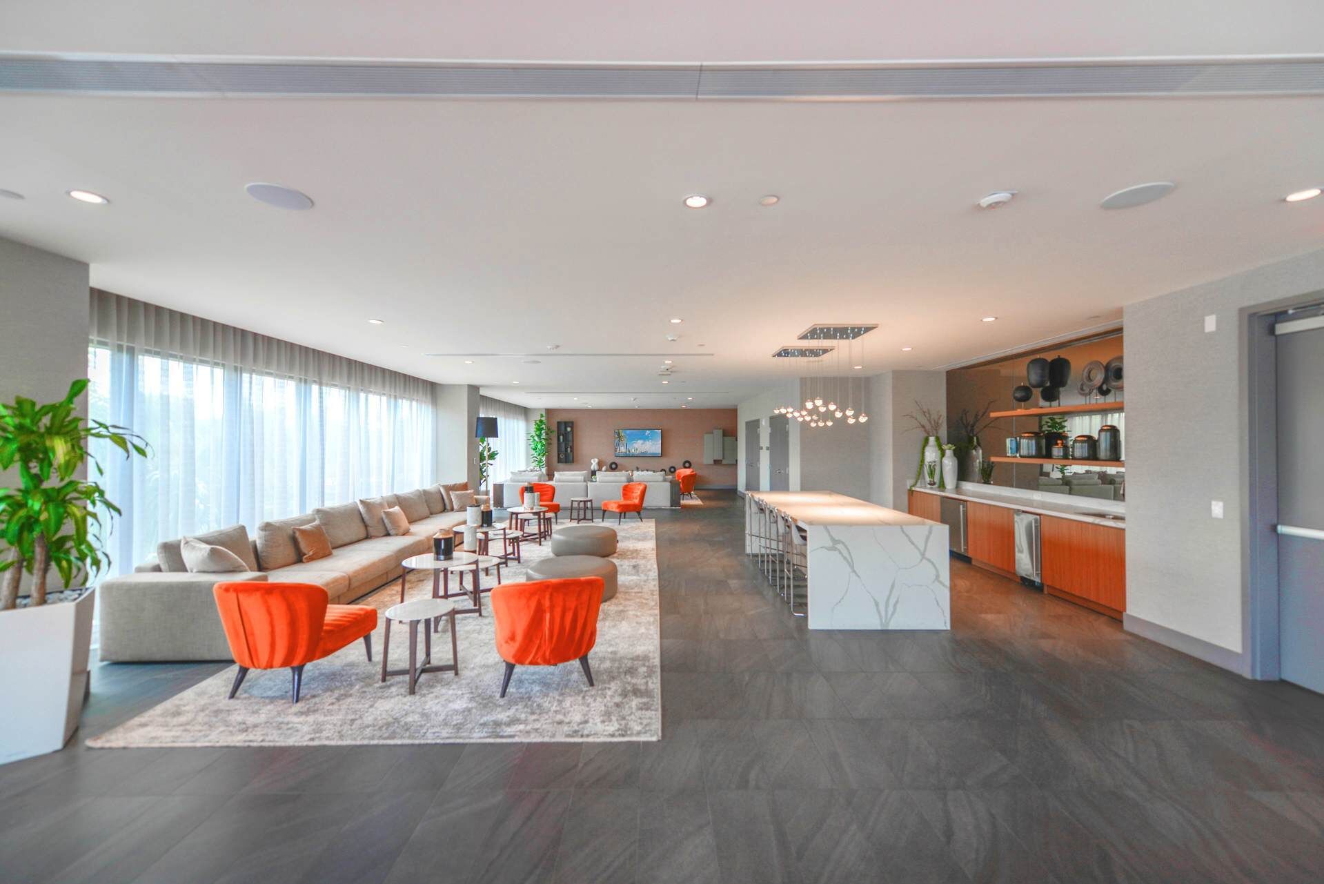 A spacious living area with a sofa, orange chairs, and a coffee table. There is a kitchen area with a bar and shelves with kitchenware.