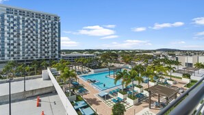 A hotel with a rooftop pool, palm trees, and a large building in the background. - Studio in the Heart of Downtown Doral | Pool (Doral)