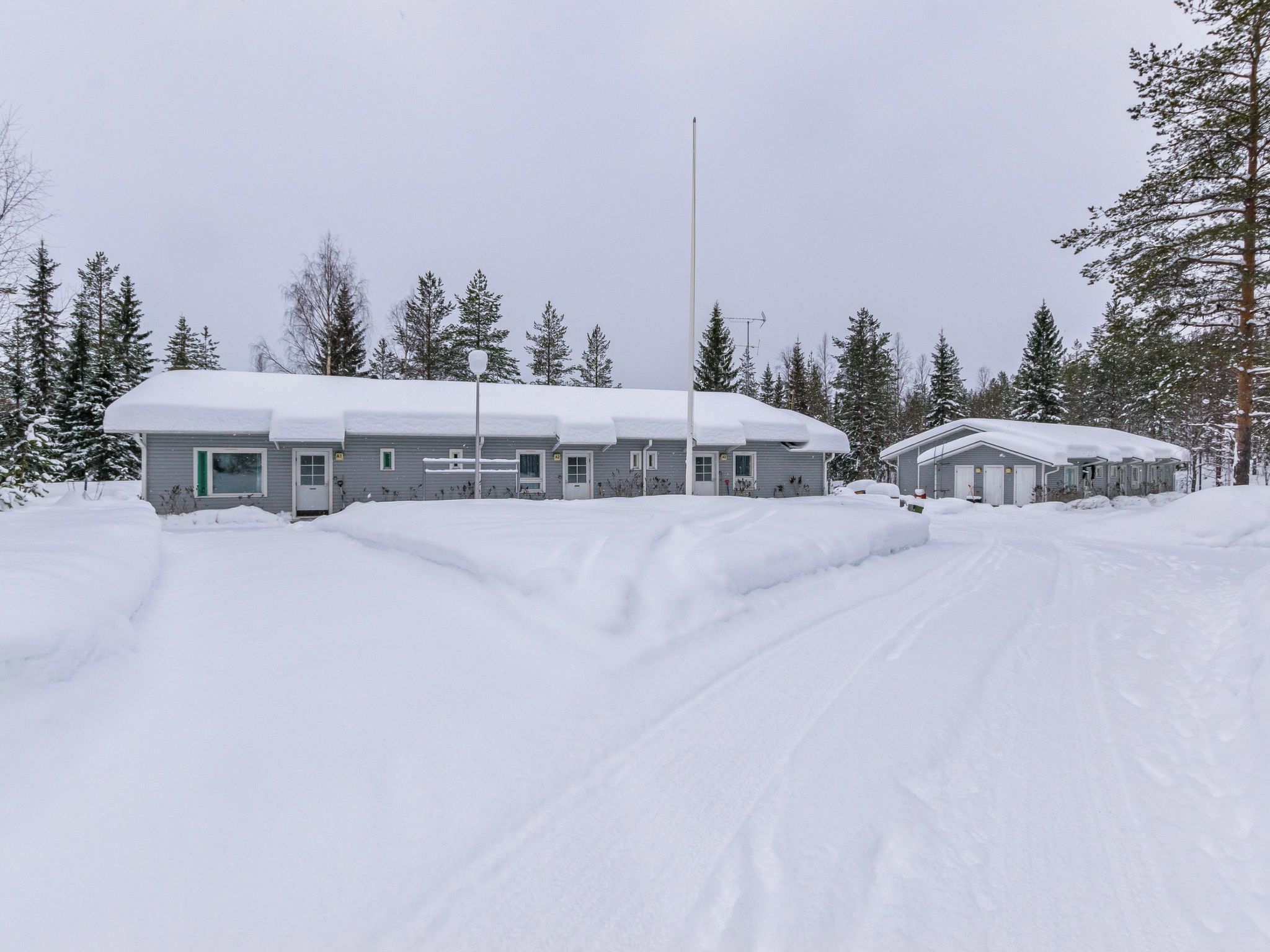 Une rangée de cabanes aux toits enneigés, entourées d’arbres.