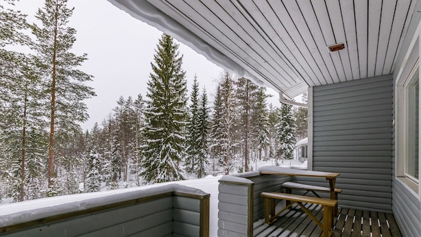 Eine Holzterrasse mit Bank und Tisch, umgeben von schneebedeckten Bäumen.