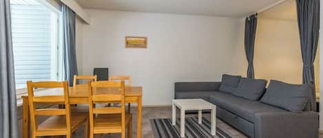 Uma sala de estar com um sofá, uma mesa de jantar com cadeiras, uma mesinha e um quadro na parede.