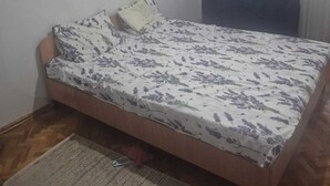 A bedroom with a bed, a chair, a window with curtains, and a wooden floor. - apartament confort in chisinau (Chișinău)