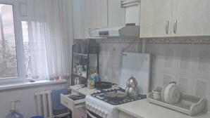 A compact kitchen with white cabinets, a stove, a sink, and a window with curtains. - apartament confort in chisinau (Chișinău)