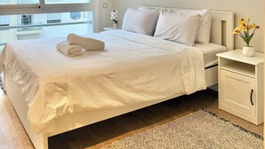 A neatly arranged bedroom with a large bed, a bedside table with a vase of flowers, and a window offering a view of the outside. - Appartement propre à Rabat – Location journalière (Rabat)