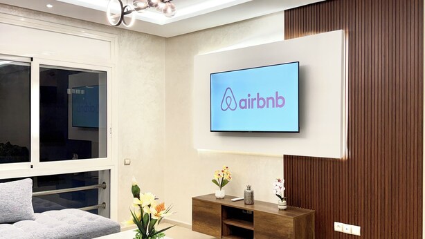 A modern living room with a grey sofa, a white coffee table, and a TV displaying the Airbnb logo. - Appartement propre à Rabat – Location journalière (Rabat)