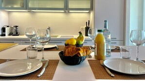 Een moderne keuken met witte kasten, een eettafel gedekt met borden, glazen en een fruitmand.