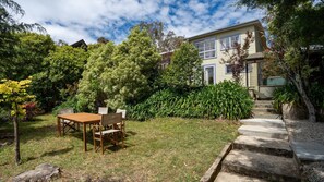 Ein Haus mit Garten, einem Holztisch und Stühlen sowie einer Treppe zum Eingang.