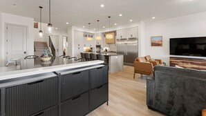 Una cocina moderna con una isla central, electrodomésticos de acero inoxidable, iluminación colgante y una zona de comedor con sillas.
