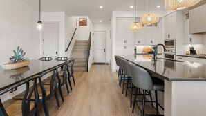 Una cocina moderna con una isla central, iluminación colgante y una escalera que sube a otro nivel.