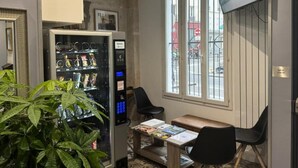 A room with a vending machine, a table with magazines, a TV mounted on the wall, and a window with a view of the street. - PARIS ROOMS & DREAMS HOTEL (Paris)