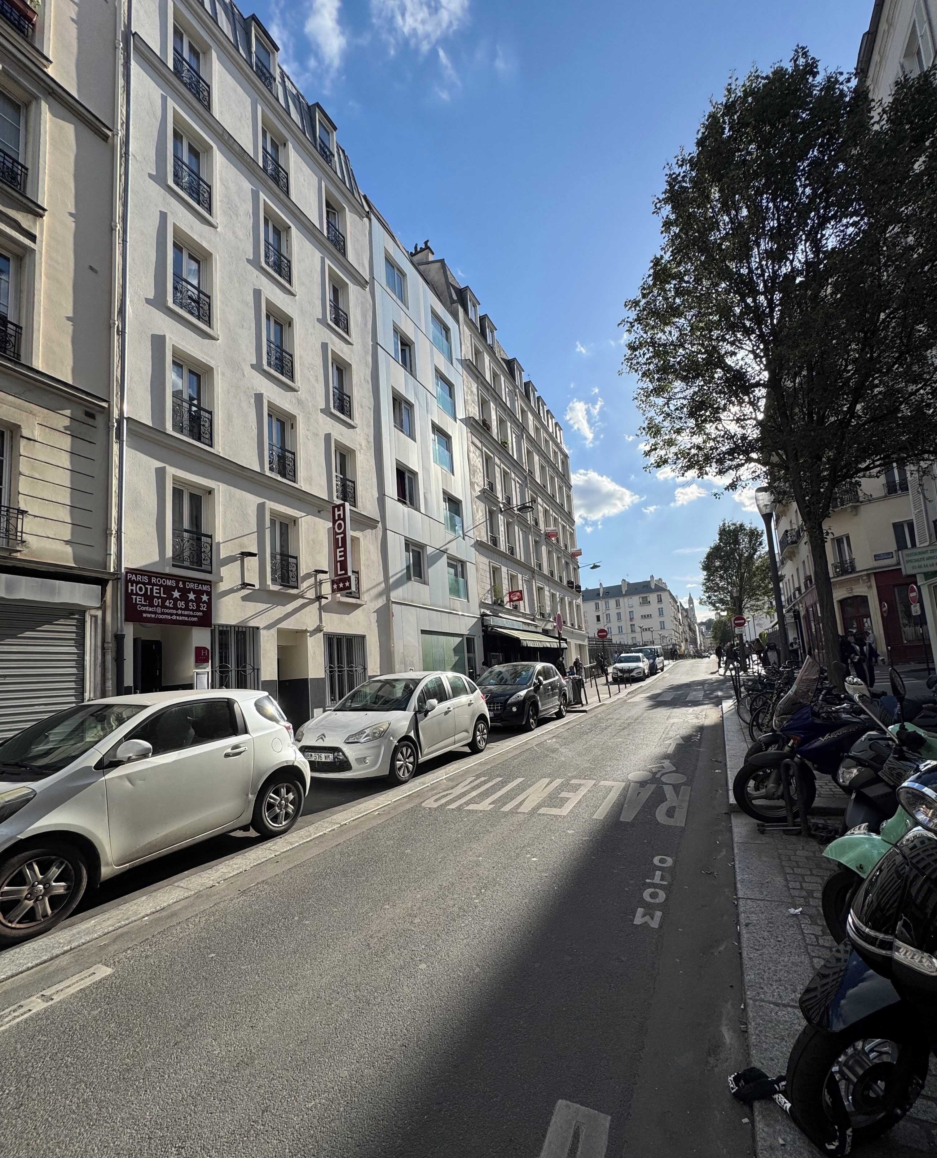 Vista de la calle con un hotel a la izquierda, llamado "Paris Rooms & Dreams Hotel", que muestra un cartel con información de contacto.