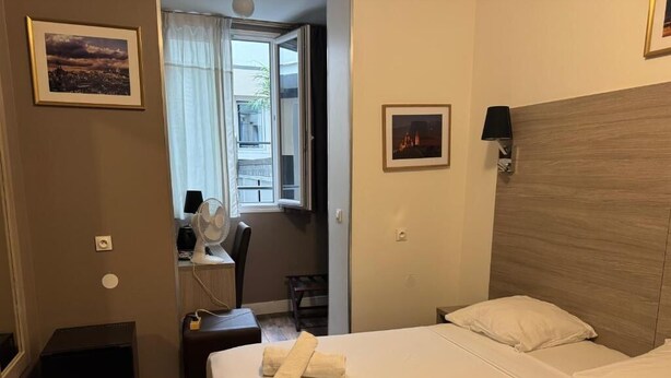 A hotel room with a bed, a desk with a chair, a window with curtains, and a wall-mounted lamp. - PARIS ROOMS & DREAMS HOTEL (Paris)