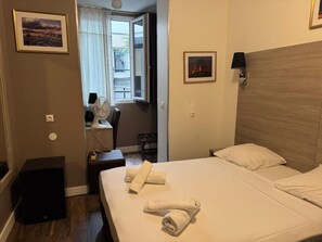 A hotel room with a bed, a desk with a chair, a window with curtains, and a wall-mounted lamp. - PARIS ROOMS & DREAMS HOTEL (Paris)