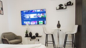 Une chambre d’hôtel équipée d’un lit, d’un téléviseur diffusant un film, d’un bureau avec deux chaises et d’un appareil de climatisation.