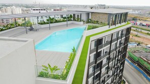 Une piscine sur le toit offrant une vue sur le paysage urbain, entourée de verdure et d’une architecture moderne.