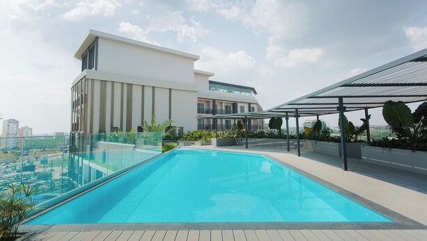 Une piscine sur le toit, dotée d’une balustrade en verre, entourée de bâtiments modernes et de verdure.