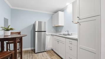 A kitchen with white cabinets, a stainless steel refrigerator, a wooden dining table, and a potted plant.