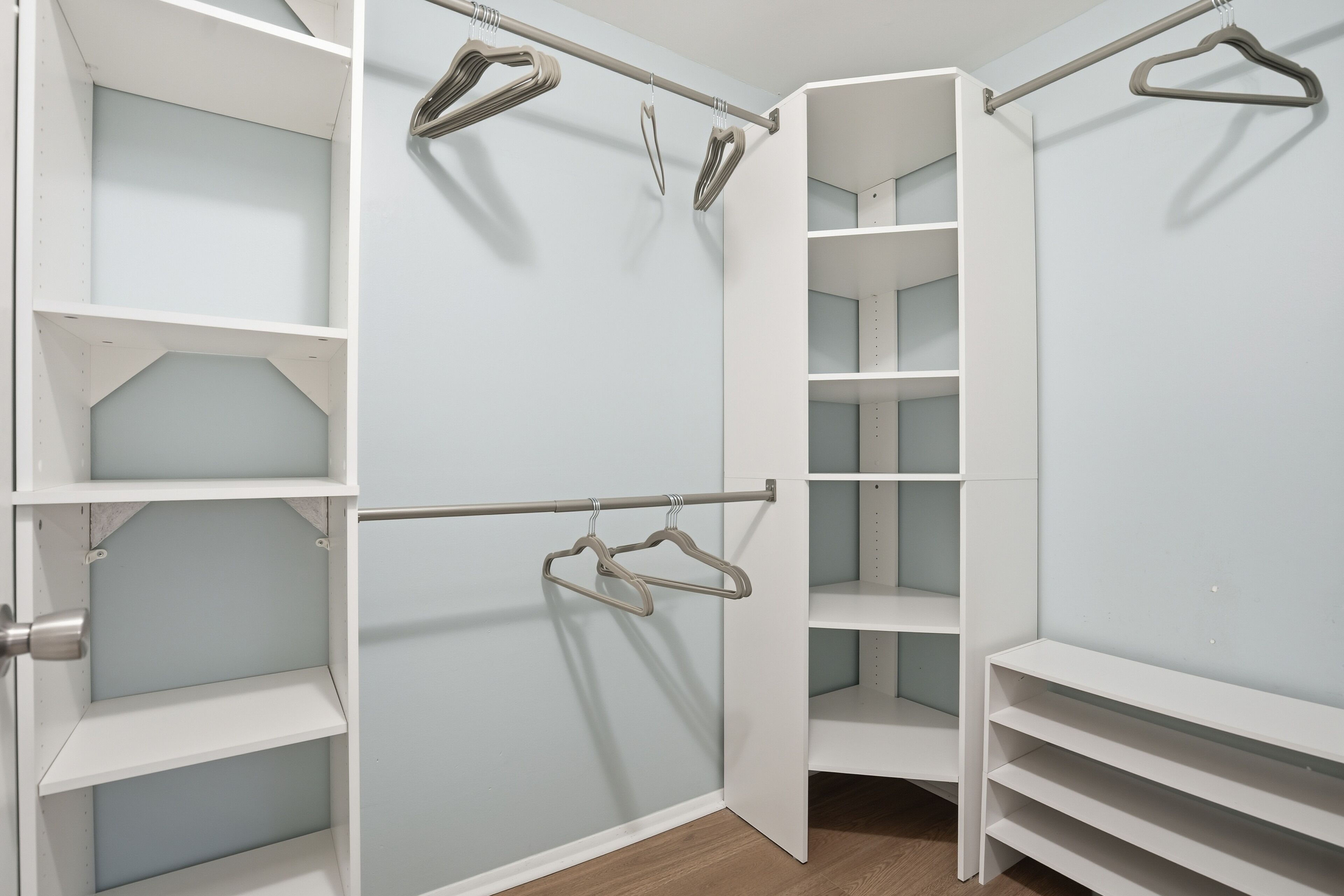 A walk-in closet with open shelving, a rod for hanging clothes, and a door leading to another room.