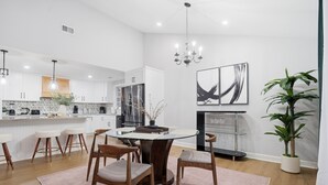 A modern kitchen with white cabinets, a central island, bar stools, and a chandelier. - Shadowlake 4BR House (Charlotte)