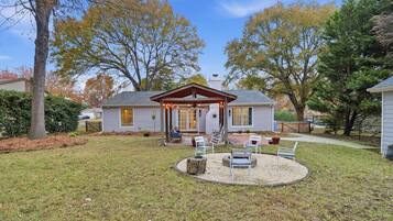 A house with a covered porch, a lawn, and trees in the background.