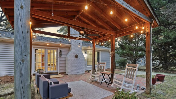 A covered patio with wooden furniture, string lights, and a brick floor. - Shadowlake 4BR House (Charlotte)