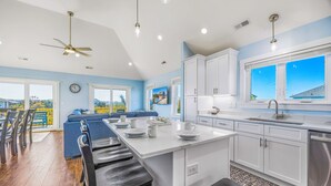 A modern kitchen with white cabinets, a large island, and a dining area with bar stools. - Oceanside, Dog Friendly Home with Private Pool and Hot Tub (Salvo)
