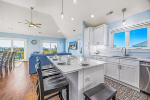 A modern kitchen with white cabinets, a large island, and a dining area with bar stools. - Oceanside, Dog Friendly Home with Private Pool and Hot Tub (Salvo)