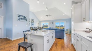 A spacious kitchen with white cabinets, a central island, and a dining area with blue upholstered chairs. - Oceanside, Dog Friendly Home with Private Pool and Hot Tub (Salvo)