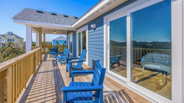 A covered deck with blue chairs and a glass door leading to a balcony with a view. - Oceanside, Dog Friendly Home with Private Pool and Hot Tub (Salvo)