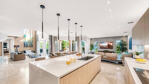 A modern kitchen with a large island, pendant lighting, and a dining area with a sofa and chairs. - Waterfront | Heated Pool | Canal View & Access | Paloma Key | VlLLAS (Fort Lauderdale)