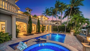A luxurious pool area with a hot tub, palm trees, and a well-lit building facade. - Waterfront | Heated Pool | Canal View & Access | Paloma Key | VlLLAS (Fort Lauderdale)
