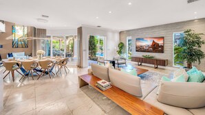A modern living room with a dining area, large windows, and a view of the outdoors. - Waterfront | Heated Pool | Canal View & Access | Paloma Key | VlLLAS (Fort Lauderdale)