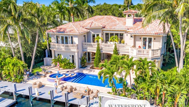 A large, two-story house with a swimming pool, surrounded by palm trees and a dock. - Waterfront | Heated Pool | Canal View & Access | Paloma Key | VlLLAS (Fort Lauderdale)