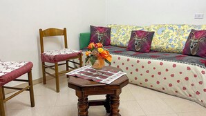 A cozy room with a wooden chair, a small wooden table with a vase of flowers, and a sofa with floral cushions. - Casa Vacanze - Villa Stefania (Pescocostanzo)