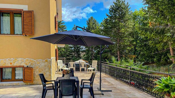 An outdoor patio with a table and chairs, a large umbrella, and a stone wall. - Casa Vacanze - Villa Stefania (Pescocostanzo)