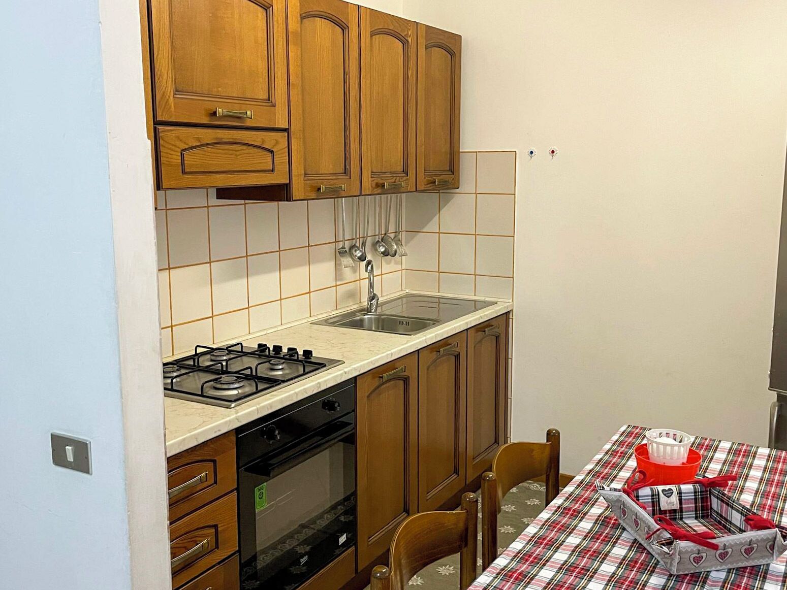 A kitchen with wooden cabinets, a gas stove, a sink, and a table with a plaid tablecloth.
