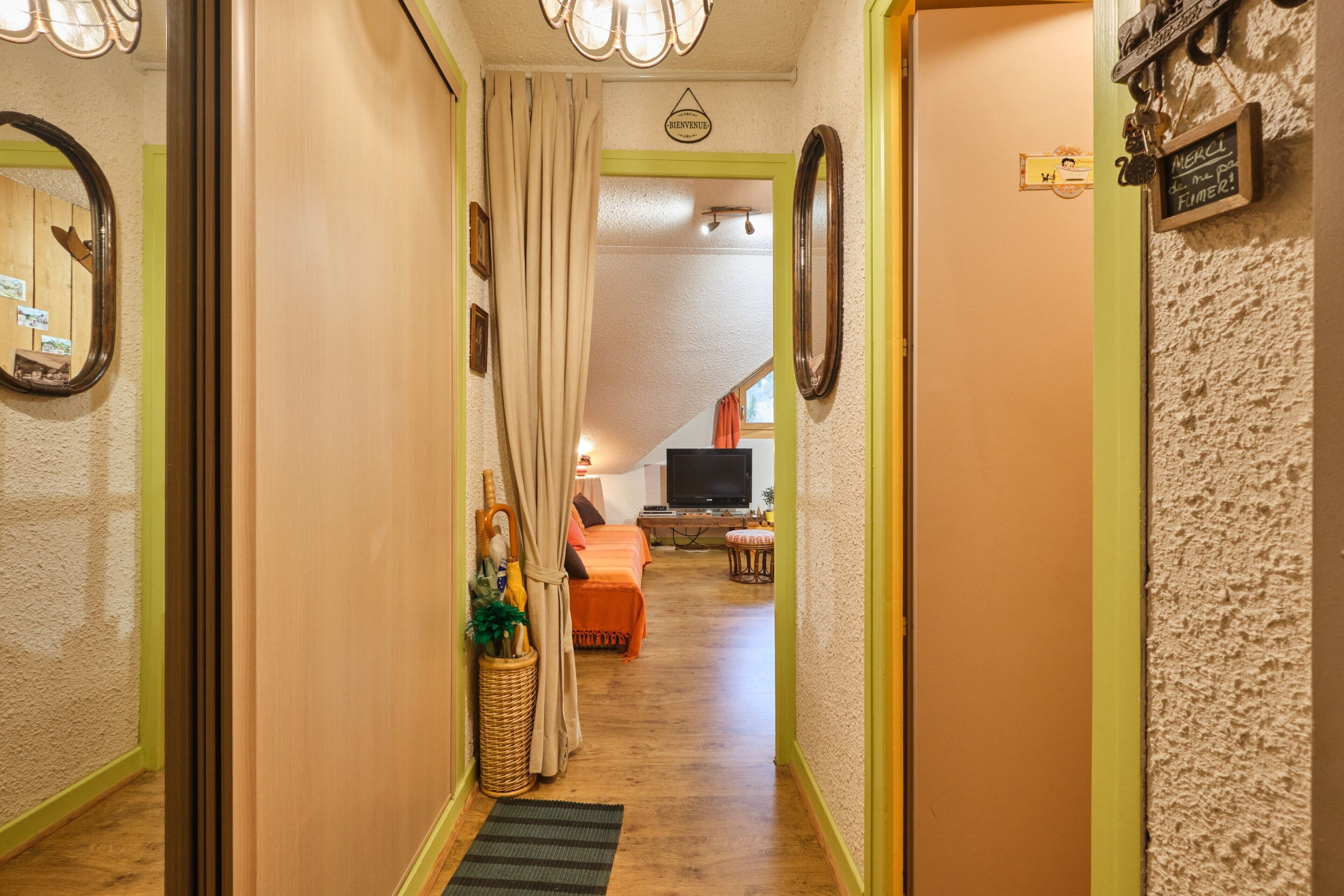 A hallway with a wooden floor, a wicker basket, a curtain, and a bed in the background.