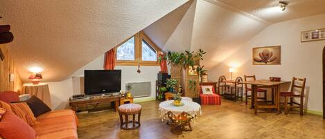 A cozy living room with a television, sofa, table, and chairs.