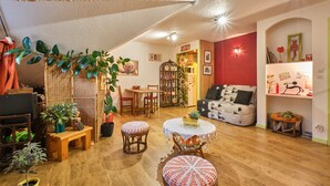 Een gezellige woonkamer met een houten vloer, een bank, een eettafel en verschillende potplanten.