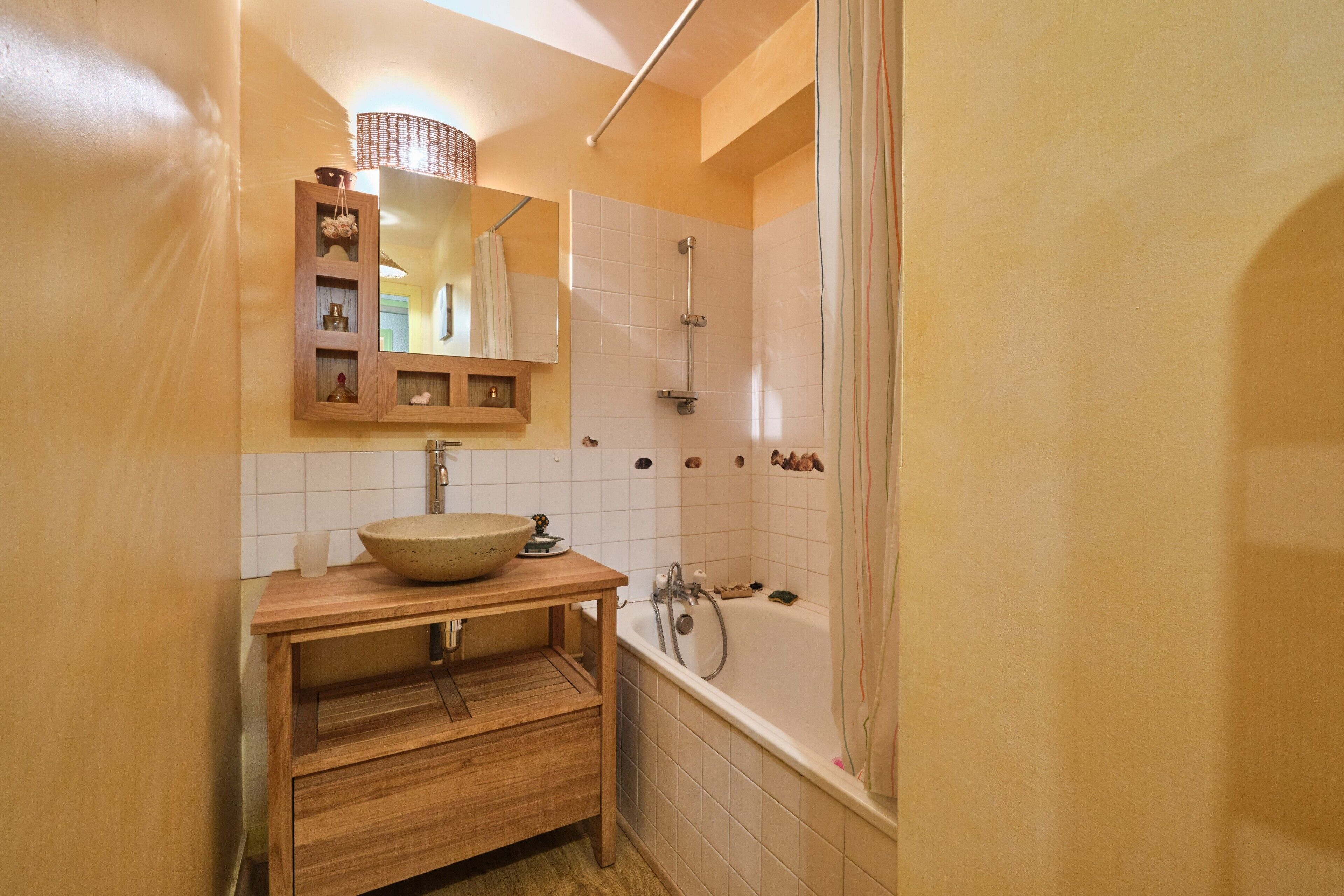 Une salle de bain avec un meuble-lavabo en bois, un grand miroir, un lavabo sur colonne, une douche et une baignoire.