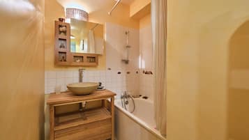 Une salle de bain avec un meuble-lavabo en bois, un grand miroir, un lavabo sur colonne, une douche et une baignoire.