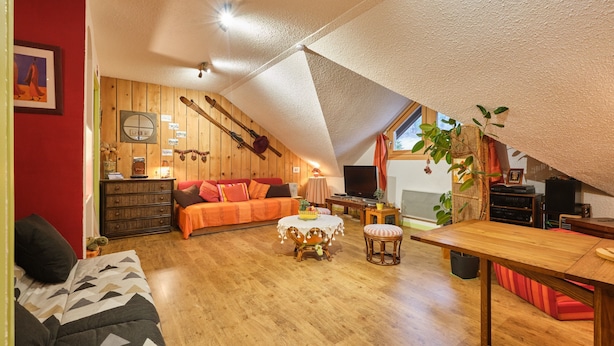 Een knus loft-appartement met een schuine kap, houten wanden, een bank, een eettafel en een televisie.